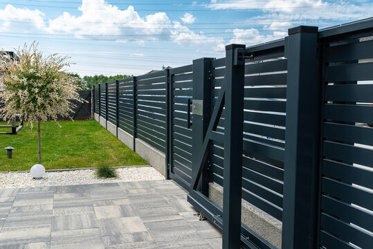 A modern panel fence in anthracite color, a visible sliding gate to the garage and a wicket with a letterbox.
