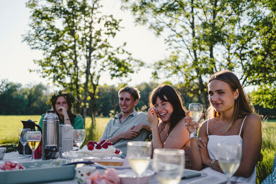 Portrait of happy young friends sitting at dining table during summer solstice brunch in back yard