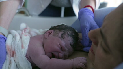 Doctor inspecting newborn baby during initial seconds of life crying on mother's chest, feeling...