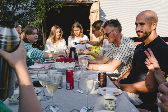 Young friends sitting at dining table in back yard enjoying brunch