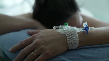 Close-up of IV drip attached at female patient hand while laid in bed at hospital