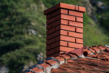 Naklejka premium The Brick Chimney. A Play of Light and Shadow on the Rooftop. Green blurry background.