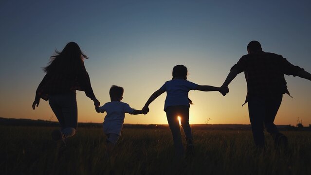 family runs across the field. happy childhood concept for little child. big happy family running across the field on the grass holding hands, sunset lifestyle on the background, silhouettes