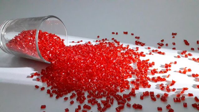 Transparent red polycarbonate masterbatch granules spill from a shot glass over a white background with dramatic light lines, this polymer is a colorant for products in the plastics industry