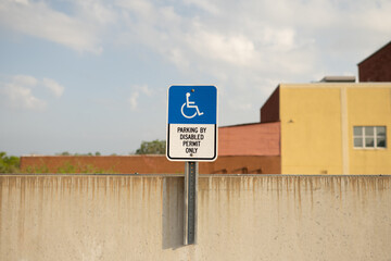 Parking by Disabled Permit Only sign attached to a concrete wall on a rooftop parking garage with a yellow building in the background, copy space