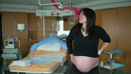 Pregnant woman having contractions standing at clinic with hospital equipment in background...