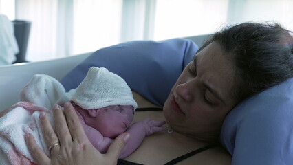 Mother holding newborn baby right after giving birth, first seconds of life of an infant resting on...