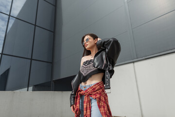 Urban fashion beautiful woman with sunglasses in a stylish black bandana top with a leather jacket and jeans posing in the city