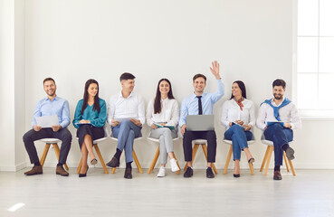 Portrait of happy smiling young man raising hand to ask or answer a question on a business meeting....