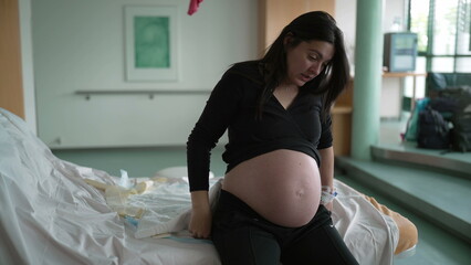 Pregnant woman suffering from contractions during pre labor at clinic covering face in pain,...