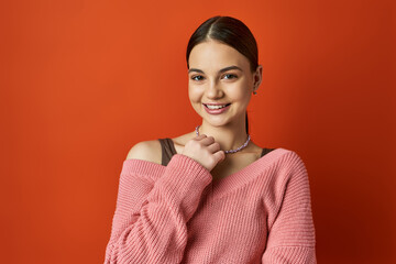 Obraz premium A brunette teenage girl in a soft pink sweater posing gracefully for a portrait on an orange studio background.