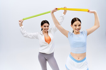 Two pretty, brunette teenage girls in sportive attire standing next to each other on a grey studio background, smiling.