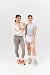 Two pretty, brunette teenage girls in sportive attire stand side by side in a studio, exuding confidence and friendship.