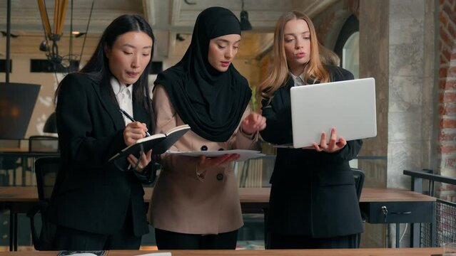 Teamwork multiracial co-workers female multiethnic colleagues girls office partnership Arabian Indian Muslim Asian Caucasian women businesswomen discuss project business laptop papers notes work talk