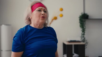 Senior female in funny sports outfit doing squats at home, striving to get fit