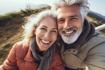 Fototapeta premium A couple of older people are smiling and posing for a picture. The woman is wearing a red jacket and scarf, while the man is wearing a green jacket. Scene is happy and lighthearted
