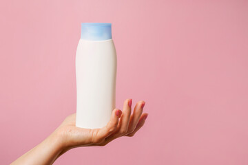 Woman Hand holding white bottle of shampoo or hair conditioner on pink background