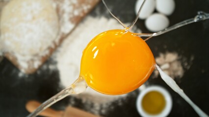 close up view of yolk falling on flour on black stone table