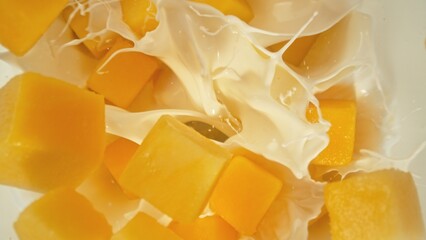 Fresh mango pieces falling into cream, top down view