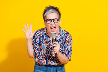 Photo portrait of attractive retired woman singing karaoke microphone dressed stylish colorful clothes isolated on yellow color background