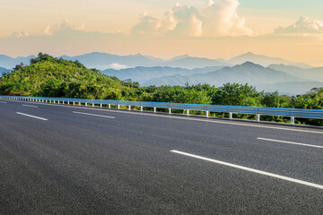 Asphalt highway road and green forest with mountain nature landscape at sunrise