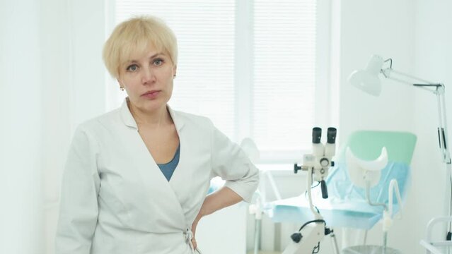 Portrait of a female doctor in the gynecologist's office. An examination chair and a colposcope can be seen behind her. High quality 4k footage