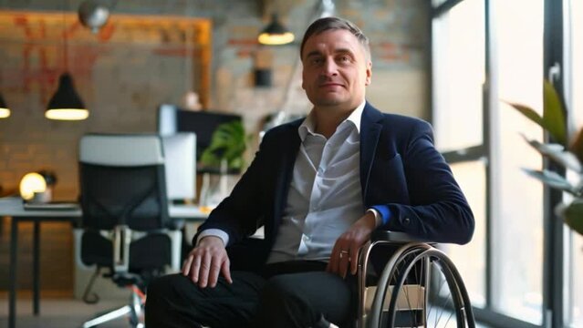 A professional man dressed in a suit is seated in a wheelchair at his office indoors.