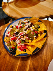 A plate of nachos with a variety of toppings including cheese, tomatoes, and jalapenos