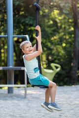 Portrait of a happy boy riding on tightrope swing in sunny green bokeh background.