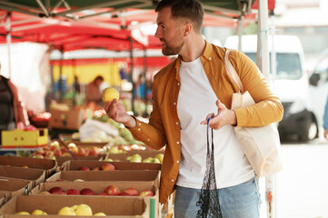 Taking an apple. Handsome man is on the street market or bazaar