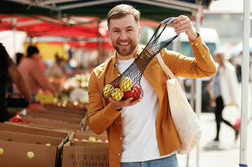 Pepper and apples, smiling. Handsome man is on the street market or bazaar