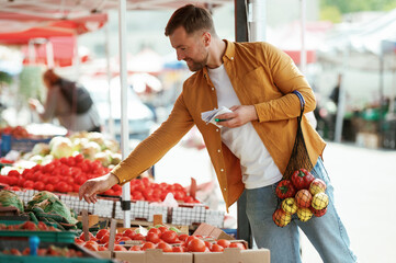 With a shopping list. Vegetables and fruits. Handsome man is on the street market or bazaar