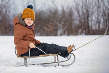 Portrait of a cute boy sitting on a sled during winter snowing
