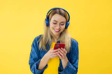 Beautiful young woman in wireless headphones listening to music on yellow background