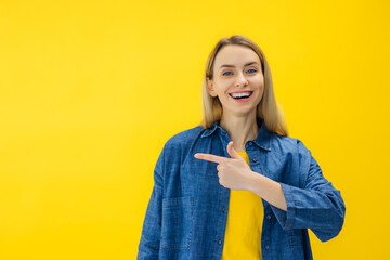 Portrait of joyful woman pointing with fingers over isolated yellow wall with copy space.