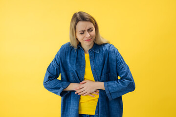girl holding hands on tummy suffering stomach ache pain isolated on bright yellow color background
