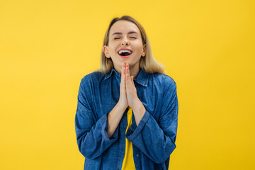 Beautiful young woman hold hands in praying gesture, isolated over yellow background