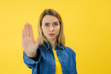 woman doing stop or denial gesture with palm isolated over yellow background