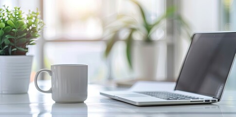 Minimalist white office desk with laptop and coffee mug on blurred background