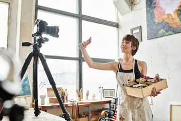 A woman elegantly presents a box of paint in front of a camera.