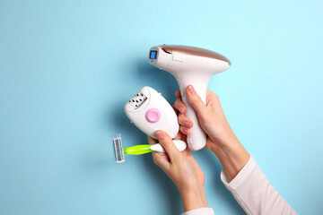 A modern epilator for removing unwanted body hair at home, wax strips, a mechanical epilator and a razor on a colored background in female hands