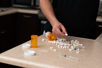 Man trying to inject a sustance with a syringe and a table full of drugs