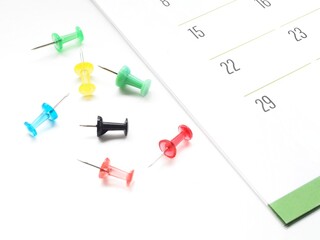 A group of unstuck colored push pins next to a monthly paper calendar for marking events or meetings