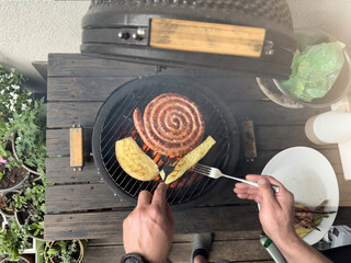 A man fries sausages and vegetables on the grill. Grilling season is open. Delicious grilled sausages close-up.