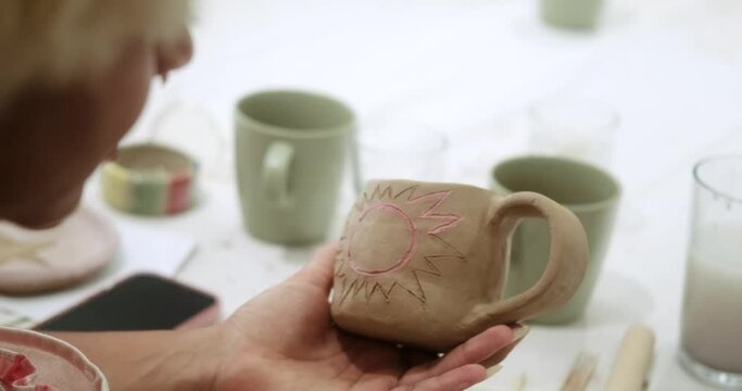 Close-up on the hands of a young African American woman who paints with a brush on a clay mug the sun with special paints. Master class for adults on hand modeling from clay in a bright workshop.