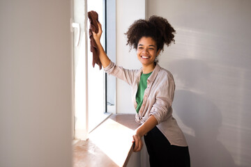afro american woman in casual clothes wipes the window with a rag
