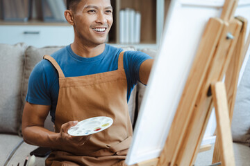 Young male artist painting on canvas in the home studio, fine arts and creativity concept.