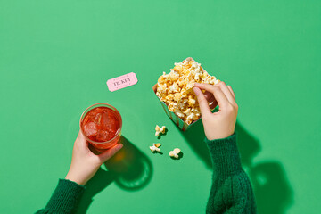 a can of soda, human hand taking the popcorn from bucket