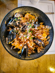 A plate of food with a lot of chopsticks on it. The plate is black and the food is a mix of vegetables and meat