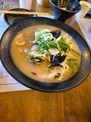 A bowl of soup with a lot of vegetables and meat in it. The soup is served on a wooden table